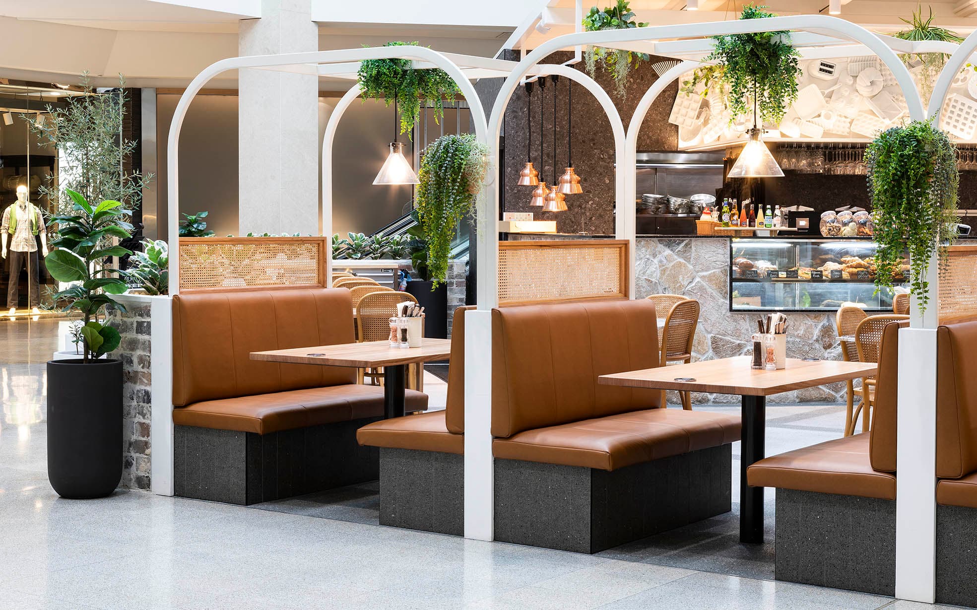 Seating area with hanging greenery and wicker backrests at Frankie B's Brunch House.