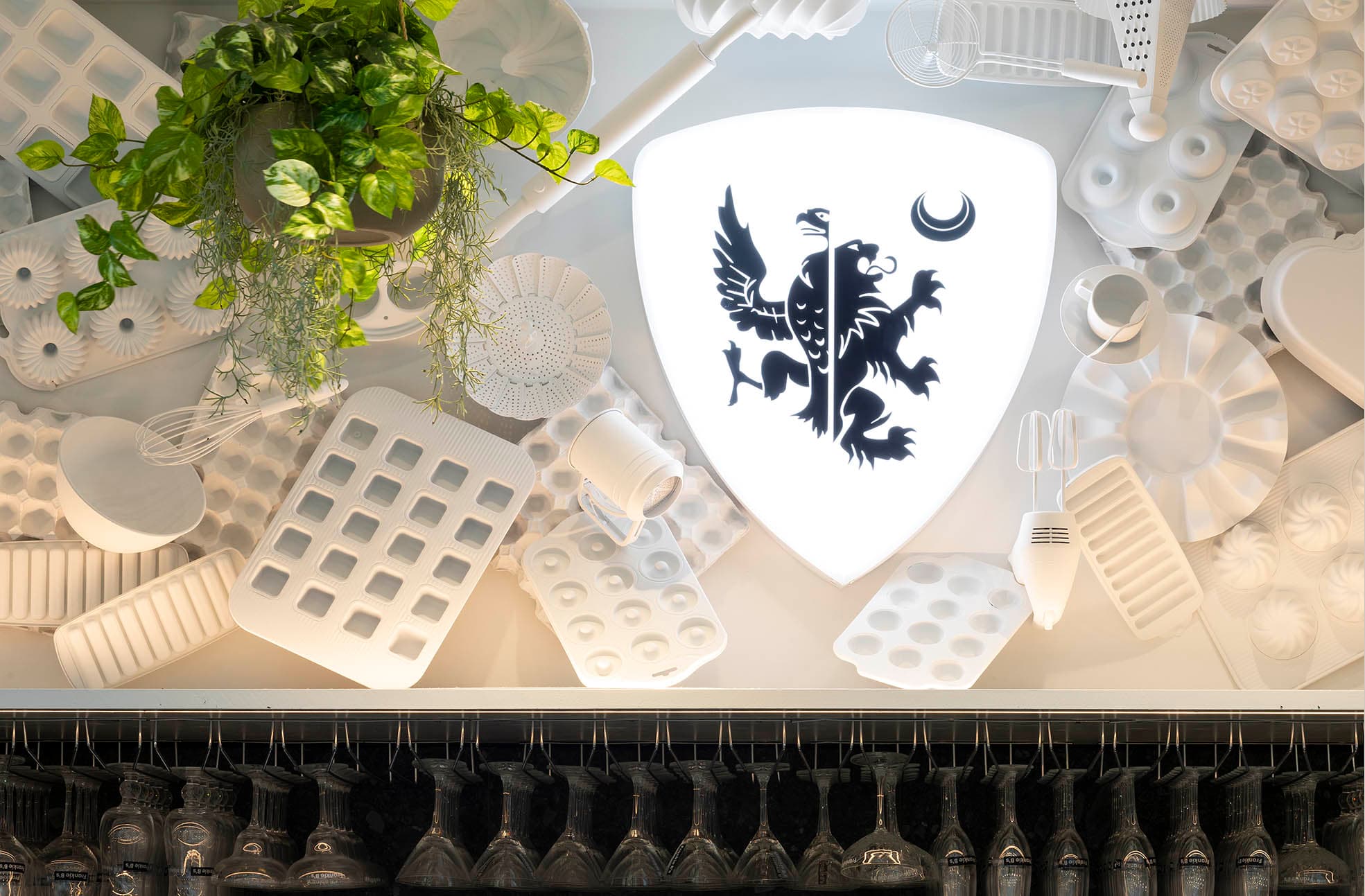 Decorative wall display with a shield emblem and kitchen utensils at Frankie B's Brunch House.