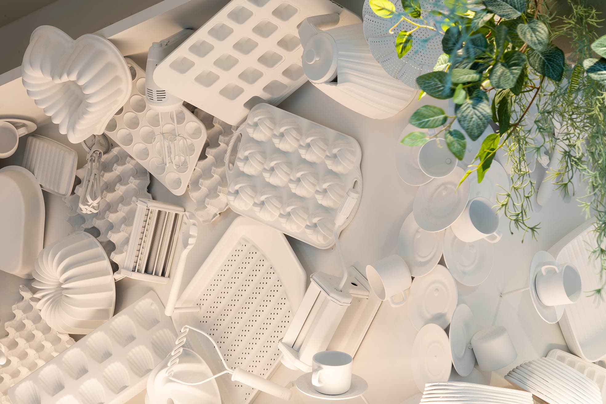 Artistic arrangement of white kitchen utensils and molds at Frankie B's Brunch House, with green foliage in the corner