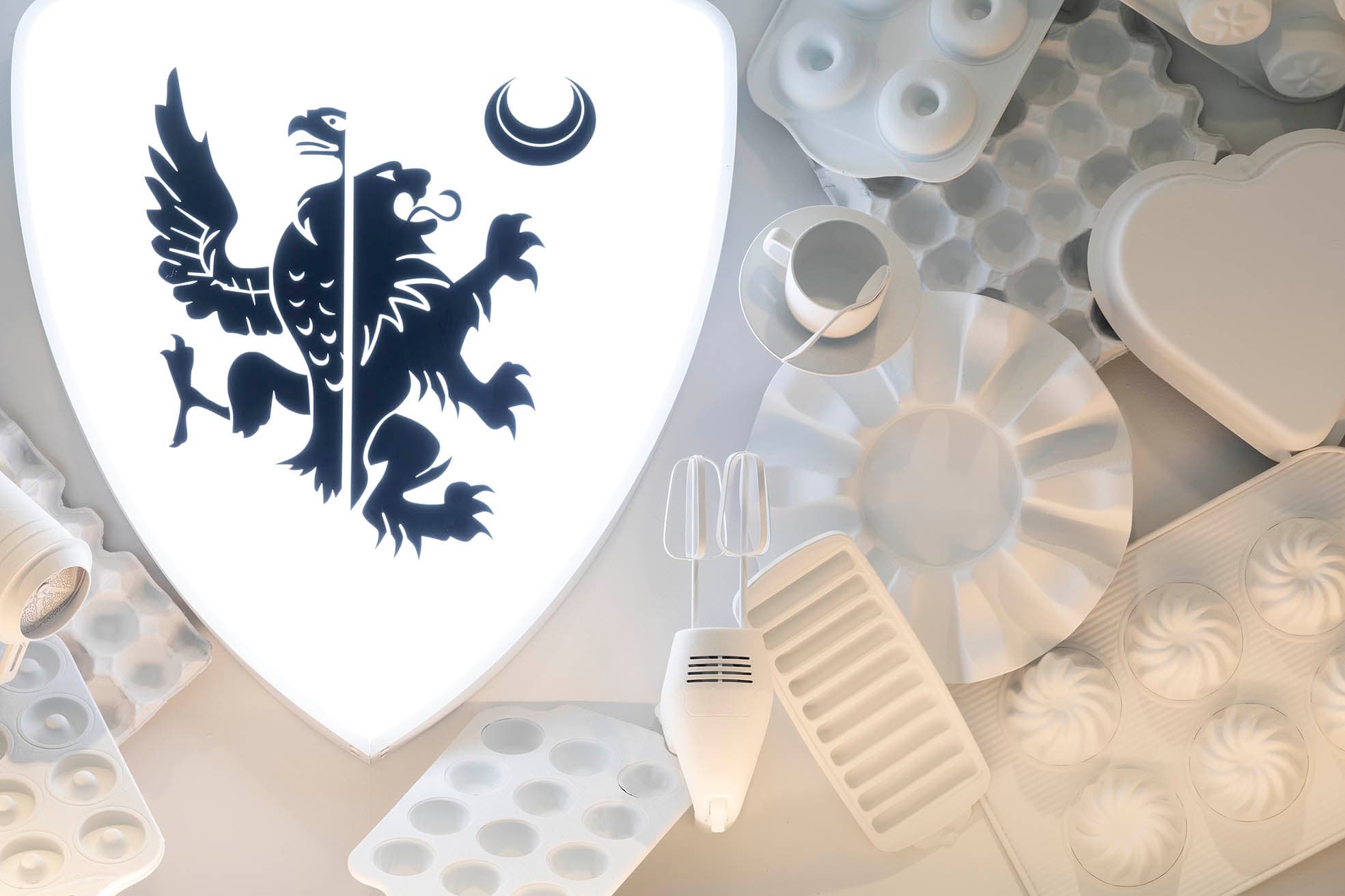 Close-up of a shield logo with a griffin and crescent moon at Frankie B's Brunch House, surrounded by white kitchen utensils and molds.