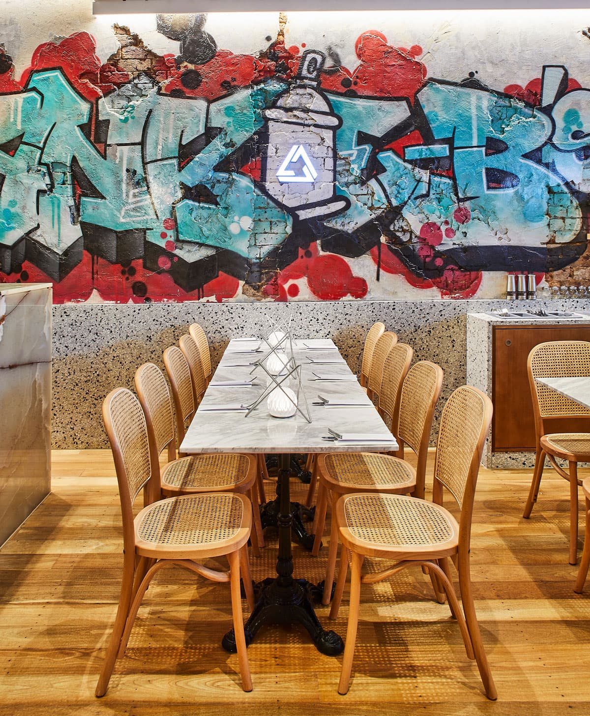 Frankie B's dining table with wooden chairs and graffiti mural background.