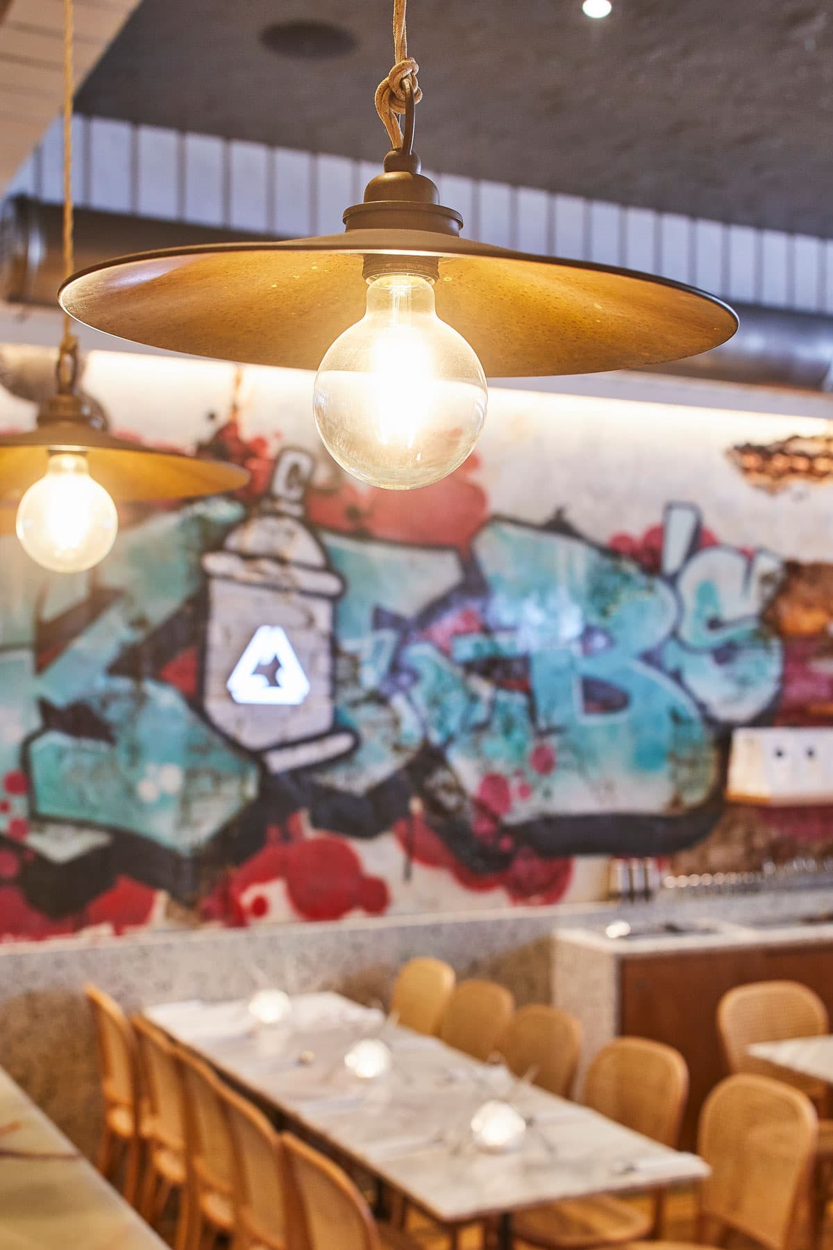 A section of Frankie B's featuring a long dining table, graffiti wall art, and hanging industrial lights